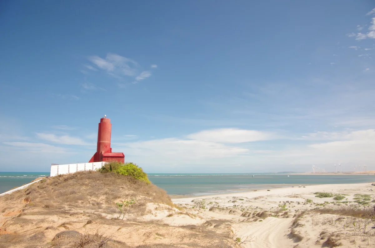 A scenic beach featuring a lighthouse, a popular kitesurfing spot with colorful kites in the sky, and a prominent sand dune providing a picturesque backdrop.