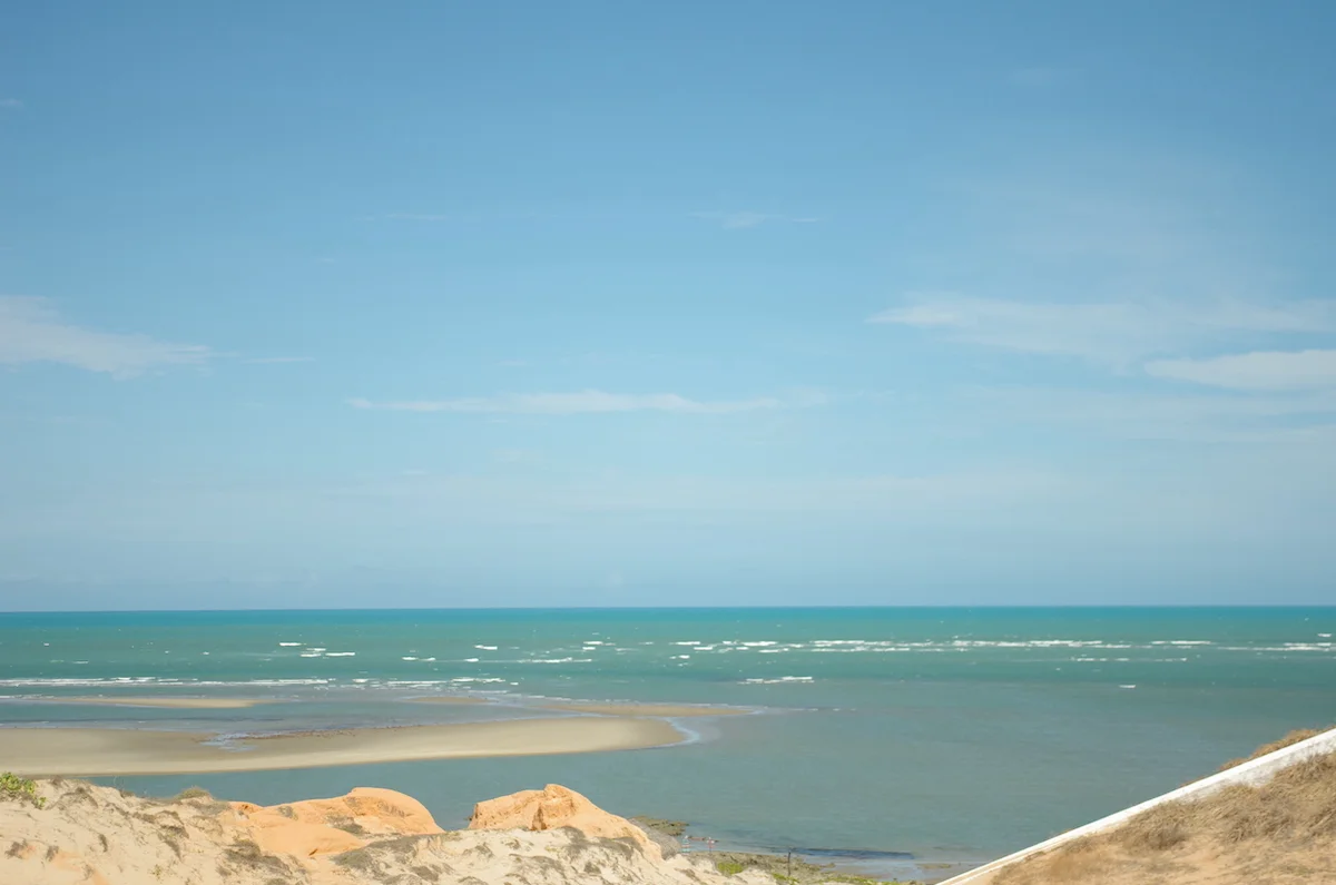 A vast ocean with white-capped waves, a designated kitesurfing area marked by colorful kites in the air, and a sprawling beach offering ample space for relaxation and recreation.