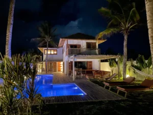 A luxurious villa in Brazil illuminated at night, featuring a spacious pool and surrounded by a beautiful garden with towering coconut trees