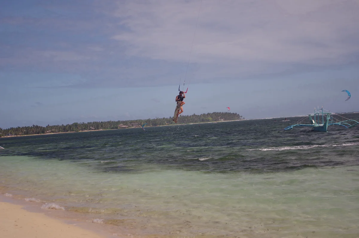 A kitesurfer jumping over blue clear water with palm trees in Siargao, Philippines.