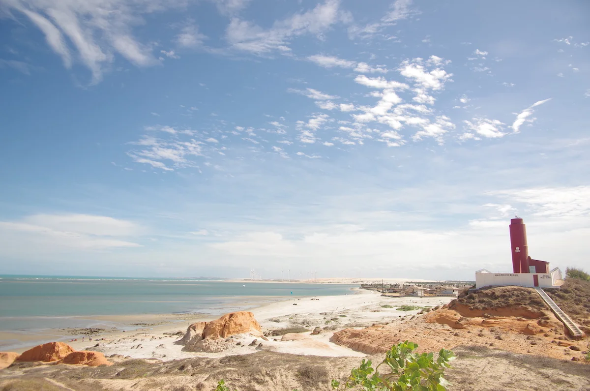 A expansive lagoon surrounded by sandy shores, a vibrant kitesurfing spot with kites soaring high, and a lighthouse standing prominently in the foreground, creating a captivating coastal scene.