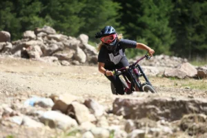 "An adventurous young woman mountain biking near Lago di Garda on a thrilling bike trail, surrounded by lush greenery and the majestic mountains of the Italian Alps."