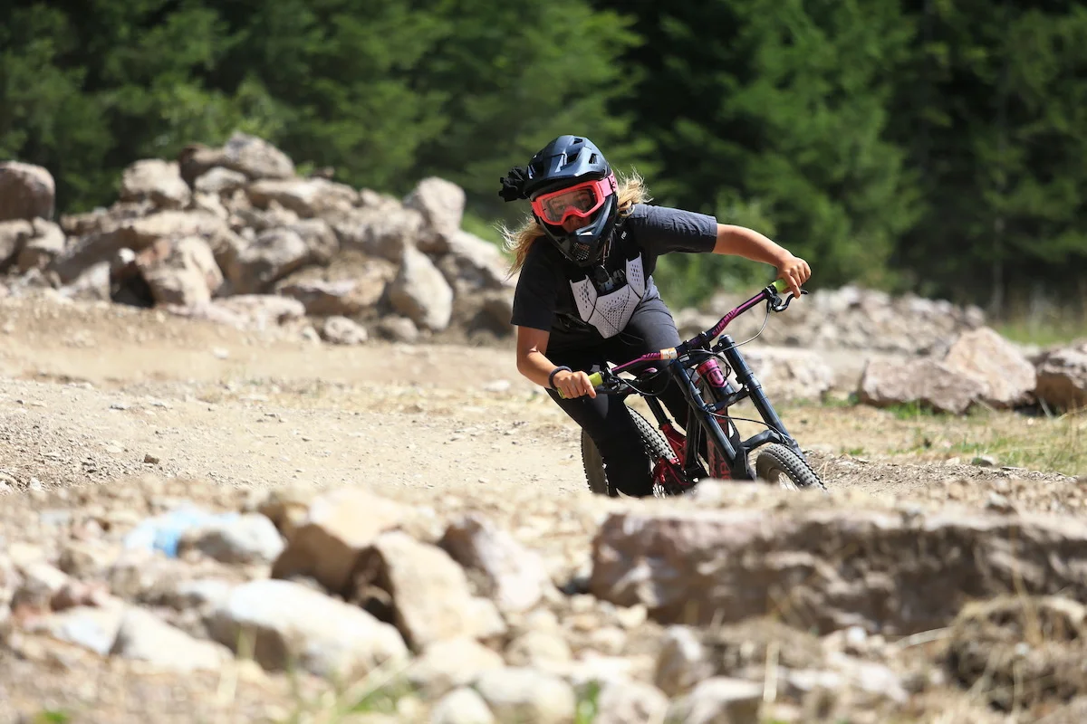 An adventurous young woman mountain biking near Lago di Garda on a thrilling bike trail, surrounded by lush greenery and the majestic mountains of the Italian Alps.