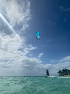 A scene of crystal-clear water with coconut trees lining the shore, and a kite surfing girl riding the waves. The perfect place for a kite camp.