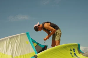 A man stands on the sandy shore, meticulously setting up his kite for an upcoming kiteboarding session. With focused determination, he attaches lines, inflates the kite, and checks the rigging, preparing himself for an exhilarating ride on the water.